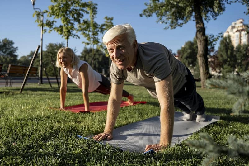 Un couple âgé en plein air effectue une séance de yoga, illustrant les bienfaits du sport sur le bien-être mental et physique des seniors